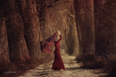 the beautiful girl with a red dress is standing between the trees
