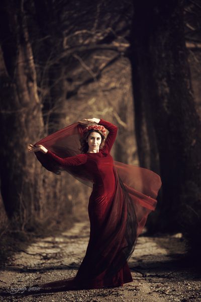the beautiful girl with a red dress is standing between the trees
