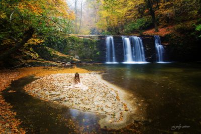 the beautiful girl with a pale dress is sitting in front of the waterfall