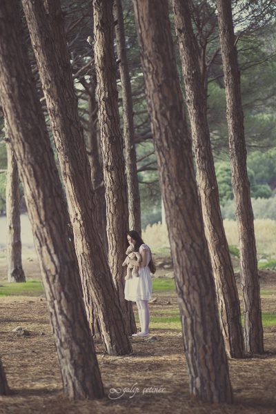the girl with a toy is standing between the trees